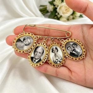 May include: A gold-toned safety pin brooch featuring four oval-shaped pendants with ornate filigree frames. Each pendant contains a black and white portrait photograph of a different person, including a man in a suit and three women.