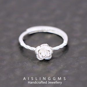 Może przedstawiać: Srebrny pierścionek z misternym wzorem róży. Pierścionek ma teksturowany pierścień i wyeksponowany kwiatowy środek. Obraz zawiera tekst "AISLING GMS Handcrafted Jewellery".