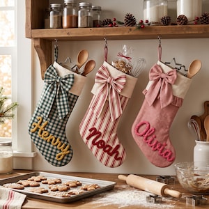 May include: Three fabric Christmas stockings hanging from a wooden shelf. The first is green and white checked with the name Henry in yellow. The second is red and white striped with the name Noah in red. The third is pink with the name Olivia in pink.