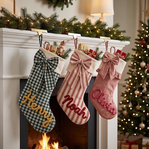 May include: Three Christmas stockings hanging from a mantel. The first is green and white gingham with the name Henry in yellow. The second is red and white striped with the name Noah in red. The third is solid pink with the name Olivia in red.
