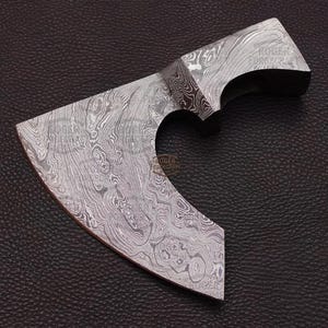 May include: A Damascus steel axe head with a curved blade and a heart-shaped cutout. The axe head has a unique pattern of swirling lines and is set against a dark, textured background.