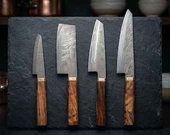 May include: Four handcrafted kitchen knives with wooden handles and patterned steel blades are displayed on a dark gray surface. The knives vary in size and blade shape, showcasing a range of culinary tools. The handles are a warm brown color.