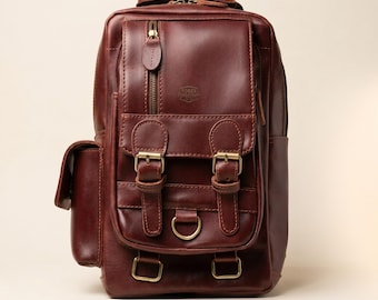 May include: A dark brown leather backpack featuring a vertical zippered pocket, a front flap with two buckle straps, a central D-ring, and two lower rectangular loops. The bag displays the embossed text ROGER CROSSCRAFT on the upper front panel.