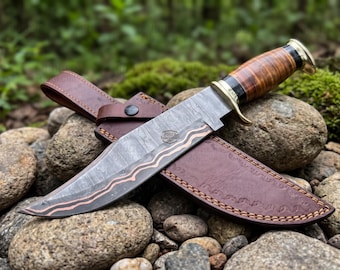 May include: A fixed-blade knife with a patterned Damascus steel blade featuring a copper wave inlay. The handle is crafted from stacked brown leather rings with black and brass accents. A brown leather sheath with decorative stitching is included.