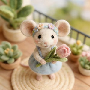 May include: A handcrafted white mouse figurine wearing a light blue dress and a floral headband. The mouse is holding a pink tulip and is standing on a woven mat. The background includes potted plants and a balcony railing.