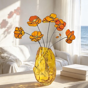 May include: A stained glass arrangement of orange poppy flowers with black wire stems and centres, displayed in a textured, translucent amber-coloured glass vase. The flowers feature vibrant orange petals with dark outlines.