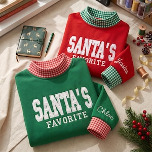 May include: Two long-sleeve sweatshirts, one red and one green, featuring a mock neck with a gingham pattern. Both shirts have the white embroidered text "SANTA'S FAVORITE" on the chest and a personalized name embroidered on the sleeve cuff.