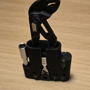 May include: A black tool organizer holding a black adjustable wrench, a silver socket wrench, and various other tools. The organizer is made of black plastic and sits on a wooden surface.