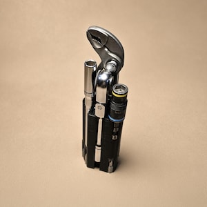 May include: A black multi-tool organizer holding a silver adjustable wrench, a metal ratchet handle, and two cylindrical sockets. One socket features a yellow ring and the text 'KLEIN', while the other has a blue ring. The tools are arranged vertically.