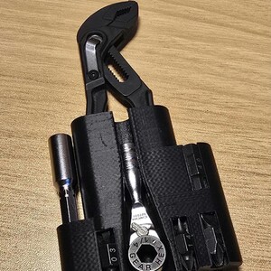 May include: A black multi-tool kit with a wrench, pliers, and various screwdriver bits. The kit includes a ratchet wrench and several hex bits. The tools are housed in a black holder.