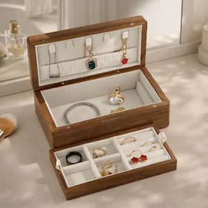 May include: A dark wooden jewellery box with an open top and a pull-out drawer. The box contains necklaces, bracelets, rings, and earrings. The interior is lined with a soft, white fabric. The box is made of dark brown wood.