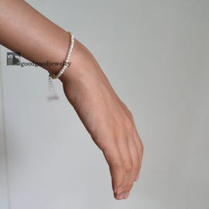 Peut inclure: Un bracelet délicat composé de petites perles blanches rondes. Le bracelet est porté au poignet. Le bijou a un design simple et élégant, adapté au quotidien ou aux occasions spéciales. Le bracelet mesure environ 17 cm de long.