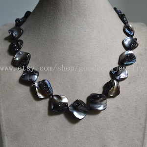 May include: A necklace with square, iridescent black beads. The beads have a lustrous, reflective quality, with hints of blue and silver. The necklace is displayed on a neutral-toned mannequin. The Etsy shop URL is visible.