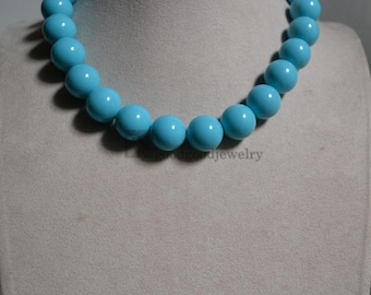 May include: A light blue beaded necklace. The necklace features large, round beads. The beads are a solid, glossy light blue colour. The necklace is displayed on a mannequin. The jewellery is a statement piece.