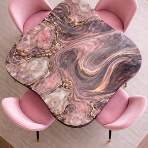 May include: A distinctive coffee table with a marble top, showcasing swirling patterns in pink, brown, and gold. Four pink velvet chairs with gold and black legs surround the table. The table's dimensions are approximately 120 cm x 80 cm.