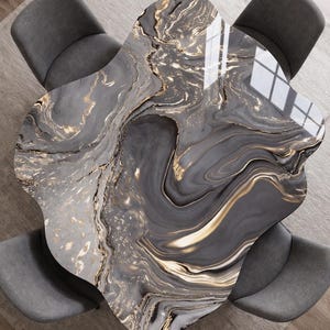 Puede incluir: Vista aérea de una mesa de centro con una forma única y una superficie con efecto mármol gris y dorado. Cuatro sillas grises rodean la mesa. La superficie de la mesa refleja la luz, resaltando su acabado brillante. Un mueble central.