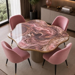 Pode incluir: Uma mesa de jantar moderna com uma forma orgânica única, com uma superfície rosa e dourada semelhante a mármore. Quatro cadeiras de veludo rosa com pernas pretas e pontas douradas circundam a mesa. A sala tem uma paleta de cores neutras com um tapete e um armário.