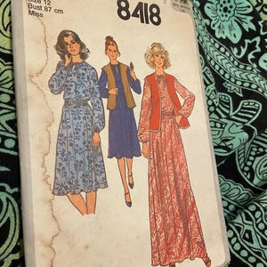 May include: A Simplicity 8418 sewing pattern envelope for size 12, 87 cm bust. The front shows illustrations of three outfits: a blue floral dress, a blue dress with a brown vest, and a red patterned dress with a red vest. The paper envelope is aged.