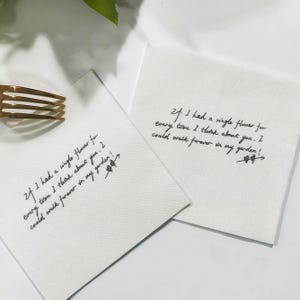 Könnte beinhalten: Zwei weiße Servietten mit handschriftlichem Text in Schwarz. Der Text lautet: „Wenn ich für jedes Mal, wenn ich an dich denke, eine einzige Blume hätte. Ich könnte für immer in meinem Garten spazieren gehen!“ Eine goldene Gabel ist sichtbar.