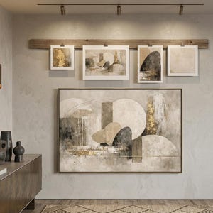 Könnte beinhalten: Innenraum in neutralen Tönen mit abstrakter Kunst. Ein großes gerahmtes Gemälde mit geometrischen Formen und Golddetails dominiert die Wand. Darüber sind kleinere Drucke an einem Holzbalken befestigt. Eine moderne Konsole und Vasen ergänzen das Ensemble.
