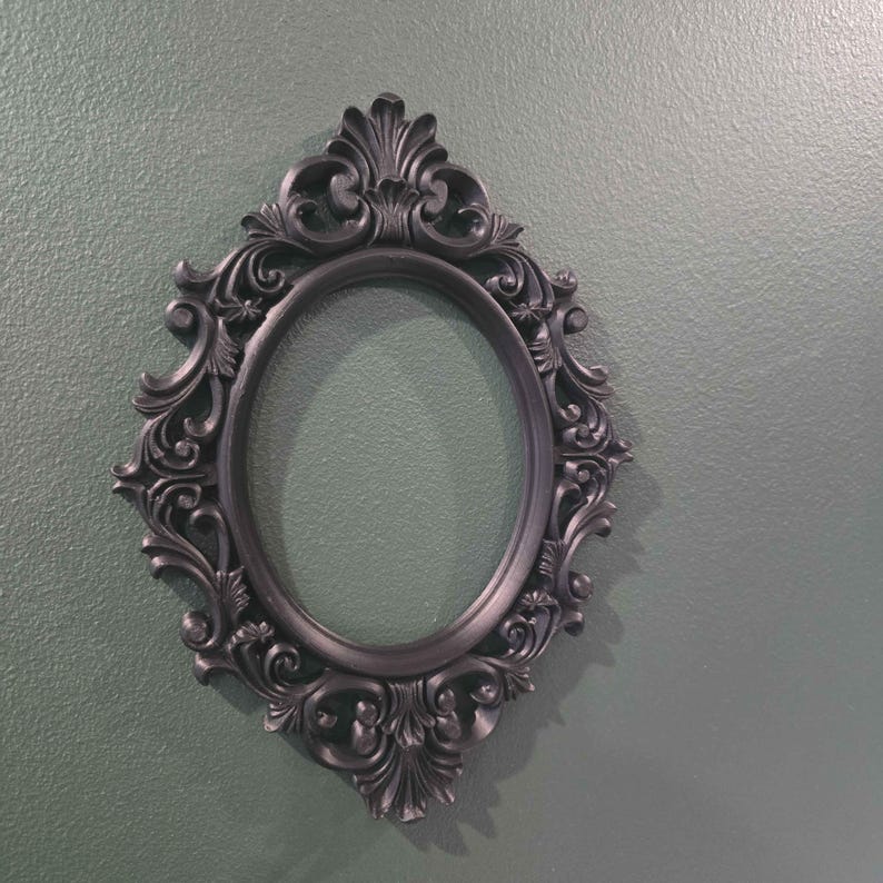 May include: An oval black picture frame with elaborate scroll detailing. The frame has a dark, matte finish and is empty. A decorative item for displaying photographs or artwork. Wall decor.