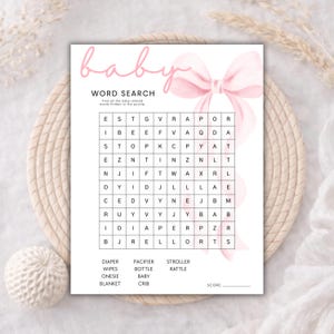 May include: A white paper sheet featuring a baby word search game with a large pink watercolor bow graphic. The text reads baby, WORD SEARCH, Find all the baby-related words hidden in the puzzle, and lists words including DIAPER, WIPES, ONESIE, BLANKET, PACIFIER, BOTTLE, BABY, CRIB, STROLLER, RATTLE, and SCORE.