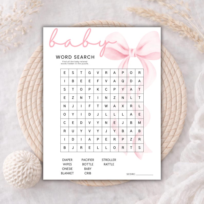May include: A white paper sheet featuring a baby word search game with a large pink watercolor bow graphic. The text reads baby, WORD SEARCH, Find all the baby-related words hidden in the puzzle, and lists words including DIAPER, WIPES, ONESIE, BLANKET, PACIFIER, BOTTLE, BABY, CRIB, STROLLER, RATTLE, and SCORE.