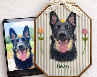 May include: An octagonal wooden framed portrait of a German Shepherd dog with a flower on its head, a pink tongue, and the name "Beau" embroidered below. The portrait is decorated with a lace bow and two embroidered flowers. A tablet displays a similar image.