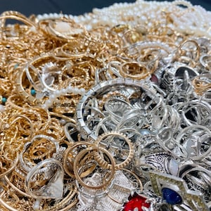 May include: A jumble of gold and silver jewellery, including rings, bracelets, and necklaces. The collection features various designs, from delicate chains to ornate rings with gemstones and pearls.