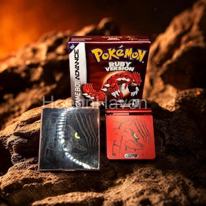 Pode incluir: Uma caixa de jogo Pokémon Ruby Version para Game Boy Advance, um console portátil vermelho correspondente com um gráfico de Groudon e um estojo protetor quadrado com uma ilustração de Groudon em preto e branco sobre uma superfície rochosa.
