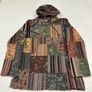 May include: A long-sleeve hooded pullover featuring a patchwork design of various earth-toned fabrics. The garment displays alternating panels of striped patterns and mushroom-themed prints in shades of brown, green, orange, and blue with black accents.
