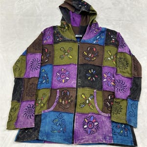 May include: A long-sleeve zip-up hoodie featuring a patchwork design of square panels in shades of purple, olive green, brown, black, and blue. The fabric is printed with black line art patterns including mandalas, Om symbols, and deities.
