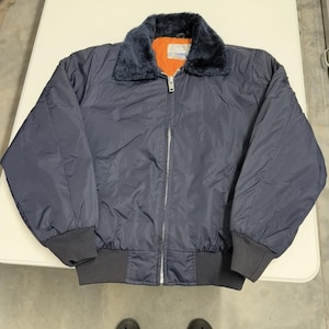 May include: A navy blue bomber jacket with a faux fur collar and an orange lining. The jacket has a zipper closure and ribbed cuffs and hem. The jacket appears to be made of a nylon or similar material.