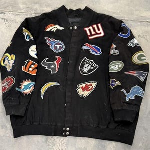 Könnte beinhalten: Schwarze Bomberjacke mit zahlreichen bunten Aufnähern mit Logos verschiedener NFL-Teams. Die Jacke hat eine Knopfleiste und einen gerippten Kragen und Bündchen. Jacke im Vintage-Stil.