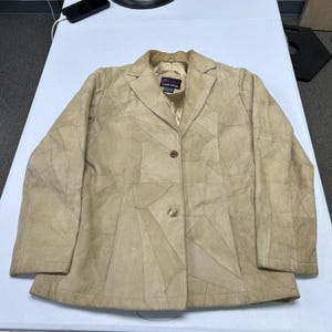 May include: A beige blazer constructed from multiple stitched leather patches. The jacket features a notched lapel, a two-button front closure, and a smooth interior lining. A label inside the collar reads Genuine Leather.