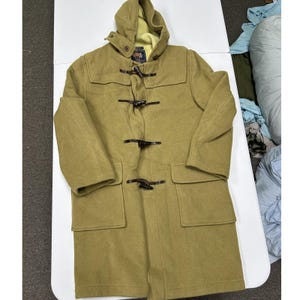 May include: A tan duffle coat featuring a hood, long sleeves, and two large front pockets. The coat is secured with four dark brown toggle closures made of wood and leather loops. The interior lining is a pale yellow color.