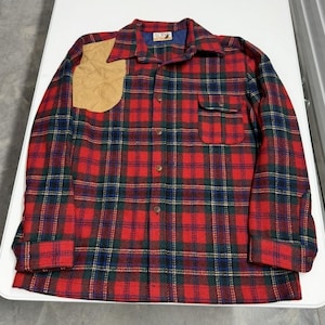 May include: A red, green, and blue plaid flannel shirt with a tan shoulder patch. The shirt has a button-down front, a chest pocket, and a collar. The shirt is made of a thick, warm material.