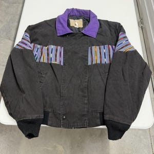 May include: A black jacket with a purple collar and colorful striped accents on the sleeves and chest. The jacket has a button-up front and black ribbed cuffs and hem. The jacket appears to be made of a durable fabric.