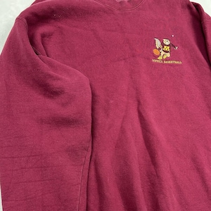 Puede incluir: Una sudadera de color granate con cuello redondo y manga larga que presenta un gráfico bordado en la parte superior derecha del pecho. El gráfico muestra un gopher de dibujos animados con un balón de baloncesto y el texto GOPHER BASKETBALL en amarillo.