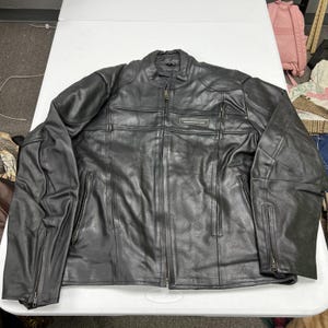 May include: A black leather motorcycle jacket featuring a mandarin collar, a full-length front zipper, and zippered pockets on the chest and sides. The jacket includes zippered cuffs and a rectangular patch on the chest with the text "SPEEDWEAR.COM".