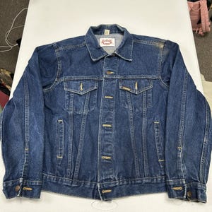 May include: A dark blue denim jacket featuring a pointed collar, long sleeves with buttoned cuffs, and a front button closure. It includes two chest pockets with buttoned flaps, two side pockets, and a white interior label reading Alabama.