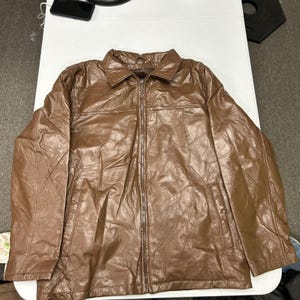 May include: A brown jacket featuring a glossy finish and a patchwork design composed of various irregularly shaped panels. The jacket includes a standard collar, a full-length front zipper closure, and two vertical slit pockets at the waist.