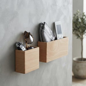 Può includere: Due contenitori rettangolari in legno chiaro montati a parete. Il contenitore più piccolo a sinistra contiene una chiave dell'auto nera e occhiali da sole con lenti marroni. Il contenitore più grande a destra contiene un tessuto a righe grigie e bianche.
