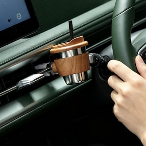 May include: A car cup holder attachment featuring a wooden exterior and a stainless steel interior, mounted onto a vehicle air vent. The cup holder includes a matching wooden lid with a small black straw inserted through the centre opening.