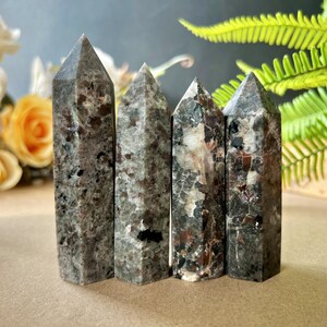 Puede incluir: Cuatro torres de cristal moteado gris y marr&oacute;n con puntas. Los cristales est&aacute;n de pie, mostrando sus patrones y texturas naturales. Los cristales son una mezcla de gris, marr&oacute;n y negro, con un acabado pulido.