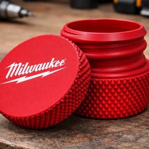 Puede incluir: Accesorio de herramienta rojo con el logotipo de Milwaukee. El accesorio tiene un agarre texturizado con patrón de diamante y un diseño atornillable. La tapa está quitada, revelando el interior de la herramienta.