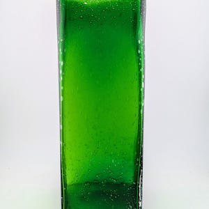 May include: A rectangular, emerald green glass vase. The vase has a slightly textured surface with small air bubbles throughout. The edges are defined and the overall shape is modern and minimalist. The vase is empty and sits against a white background.