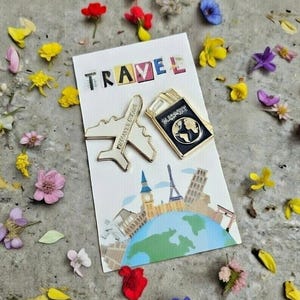 May include: A white card with the word "TRAVEL" in colorful letters, featuring an airplane and passport pin. The card depicts landmarks around a globe. The image is surrounded by colorful flower petals.