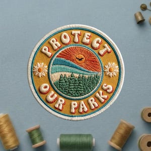 May include: Embroidered patch with the words "PROTECT OUR PARKS" in white, arched around a central design. The design features a rising sun, mountains, and trees in shades of orange, blue, and green, with two daisy accents.