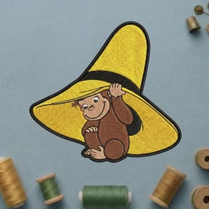 May include: Embroidered patch featuring a brown monkey holding a large yellow hat with a black band. The monkey is smiling. The patch is on a light blue background with spools of thread.